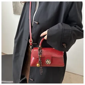 Dettaglio di una borsa a tracolla rossa vintage con chiusura dorata e ciondolo decorativo