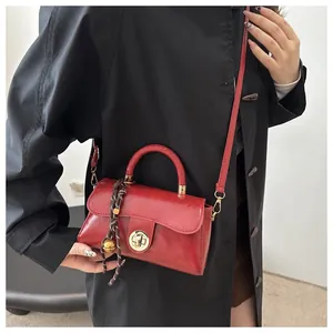 Dettaglio borsa a mano in pelle rossa lucida con chiusura dorata e pendente intrecciato