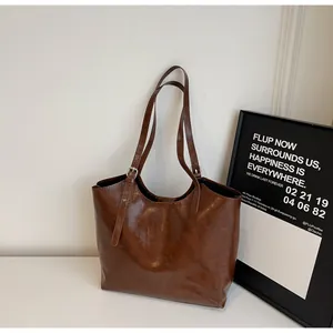 Detail view of large dark brown tote bag with glossy faux leather and buckle strap