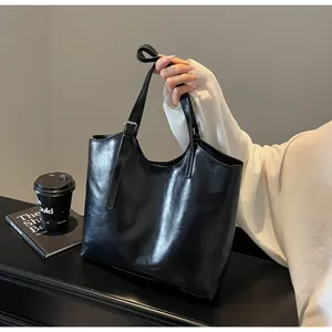 Close-up of black glossy oil-wax leather tote bag with silver buckle and coffee cup