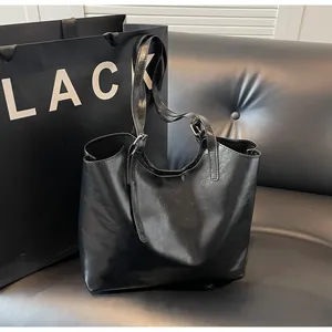 Detail view of black oil wax leather tote bag on leather sofa with black shopping bag