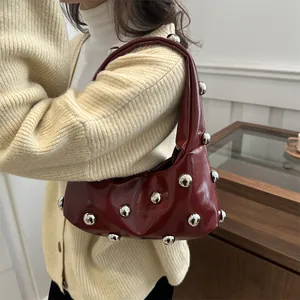 Deep red hobo bag with silver studs and glossy finish worn as a shoulder bag