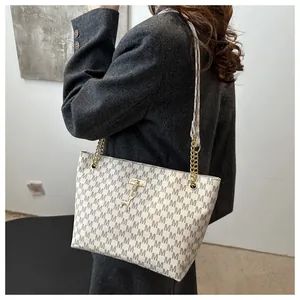Detail of white tote bag with M-pattern, gold chain strap, and deer charm on a grey blazer