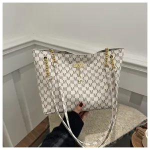 Detail of off-white tote bag with M-pattern, gold deer pendant, and chain shoulder strap