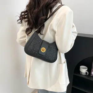 Sac à bandoulière pailleté noir avec fermoir doré porté sur une veste blanche