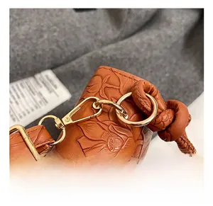Detail of golden metal hook and floral embossed texture on brown leather crossbody bag