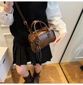 Detail of dark brown Boston bag with shoulder strap and stylish woven rope pendant