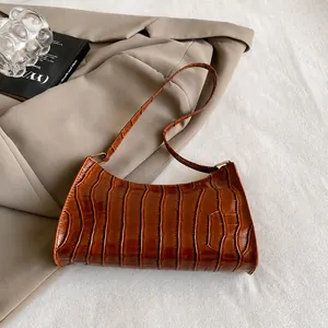 Détail de la texture crocodile sur le sac baguette en cuir PU marron sur blazer beige