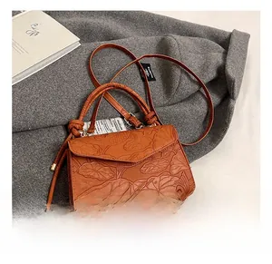 Close-up of brown leather handbag with embossed lotus and fish patterns and crossbody strap