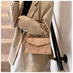 Detailed close-up of a beige crossbody bag featuring lotus and koi fish embossed patterns