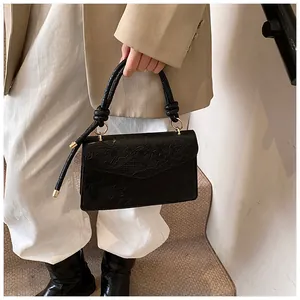 Close-up of black leather handbag with floral embossed texture and knotted gold handle