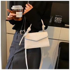 Detail of white embossed leather small square bag with floral patterns and woven handle