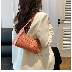 Gros plan sur un sac baguette rose-orangé à motif crocodile porté par une mannequin