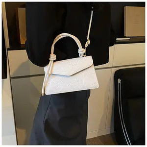 Close-up of white crossbody bag with floral embossed pattern and knotted handle detail