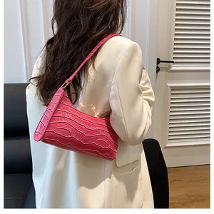 Gros plan d'un sac baguette rose rouge à motif crocodile sur l'épaule du modèle