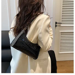 Détail du sac baguette noir motif crocodile porté avec un blazer blanc