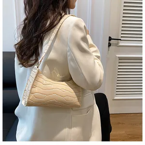 Détail du sac hobo crème à motif crocodile porté à l'épaule par un mannequin en blanc