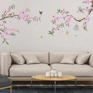 Vinilo decorativo de cerezo rosa con pájaros y jaula sobre el sofá beige en el salón