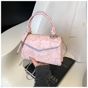 Detail view of pink crossbody bag showing floral lotus embossing and knotted handle
