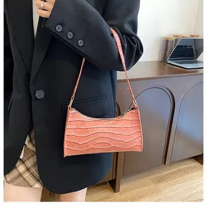 Sac baguette rose à motif crocodile porté avec un blazer noir dans un décor intérieur
