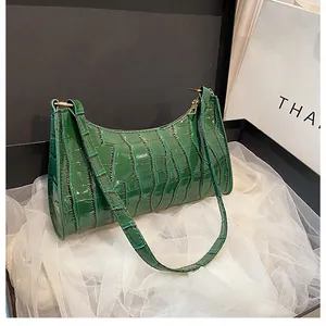 Détail du sac baguette vert foncé à texture crocodile avec zip doré dans un coffret