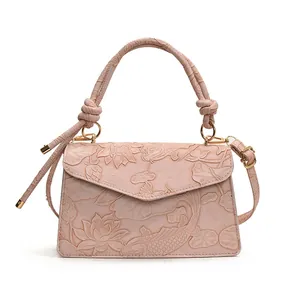 Pink crossbody handbag with embossed lotus and koi pattern and woven handle on white background