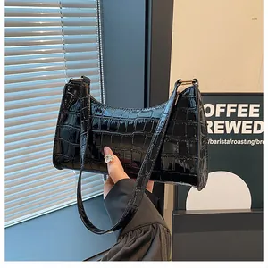 Détail de l'effet crocodile brillant noir sur un sac baguette avec fermoir doré chic