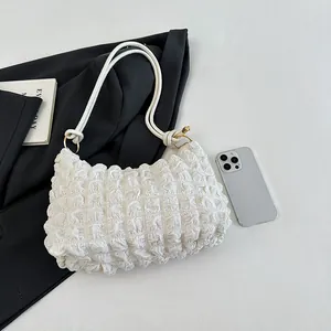Sac à épaule blanc matelassé avec texture gaufrée et détails dorés près d'un mobile