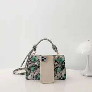 Green snakeskin pattern flap handbag with knot handle and gold hardware on a desk