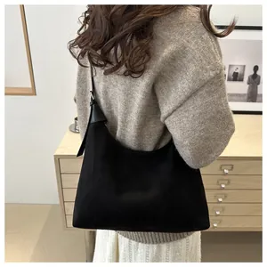 Detailed view of black suede half-moon tote bag worn by a model in a cozy interior setting