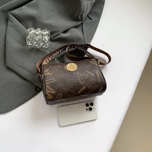 Brown cylinder bag with letter print, round gold logo and adjustable wide strap