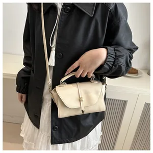 Detail of cream crossbody bag with flap closure and golden metal ring hardware on a model