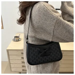 Detail of a chic black baguette bag featuring monogram print and a leather bow detail