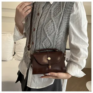 Detail of a dark brown crossbody bag with round metal buckle and leather texture