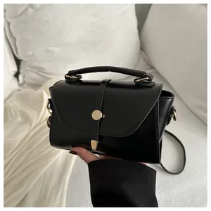 Detail of glossy black square bag with gold metal buckle and leather shoulder strap