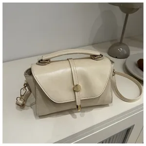 Detail of cream-colored leather crossbody bag with golden buckle and textured finish
