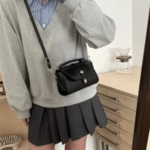 Minimalist black leather crossbody bag with gold buckle shown on a model in a cozy room