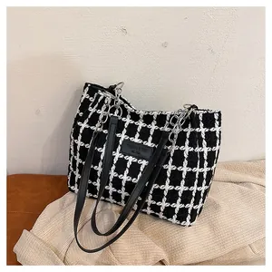 Detail view of houndstooth plaid fabric and black leather embossed patch on large tote bag