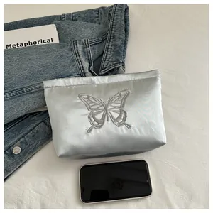 Detailed view of butterfly embroidery on a sleek satin pouch next to a smartphone