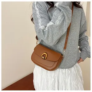 Detail of a brown leather saddle bag with a golden horseshoe buckle and stitching