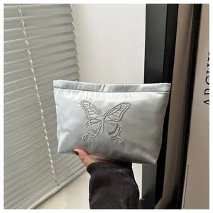 Detail of elegant light blue satin cosmetic bag featuring delicate white butterfly embroidery