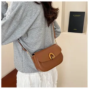Detail of a brown saddle bag featuring a gold U-shaped buckle and smooth leather finish