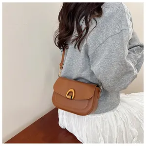 Brown leather saddle bag with golden U-buckle worn by a model in a minimal setting