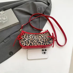 Leopard print crossbody bag with red patent leather accents on a minimalist background