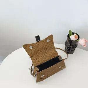 Piccola borsa quadrata marrone con monogramma e tracolla a catena su un tavolo bianco