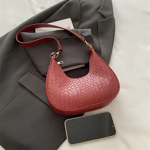 Brick red hobo bag with woven texture, crescent shape, and gold hardware on blazer background