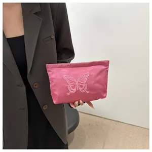 Detail of pink satin clutch bag featuring intricate butterfly embroidery held by a model