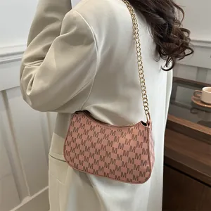 Pink crescent underarm bag with letter pattern and gold chain strap shown on model