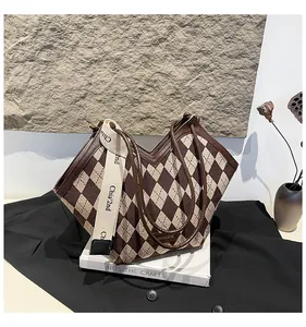 Dettaglio della borsa tote a rombi con profili in pelle e ampia tracolla su libri bianchi