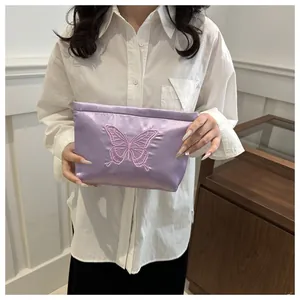 Detailed embroidery of pink butterfly on purple satin fabric vanity pouch held by hand